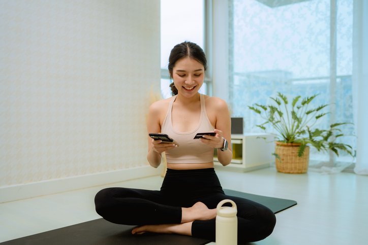 Young woman does yoga at home, paying down her credit card debt on her smartphone with her tax refund.