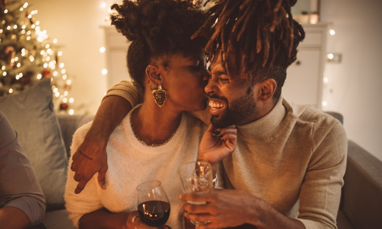 A young couple embrace in a kiss as they sit on a couch together at a New Year's Eve party. 