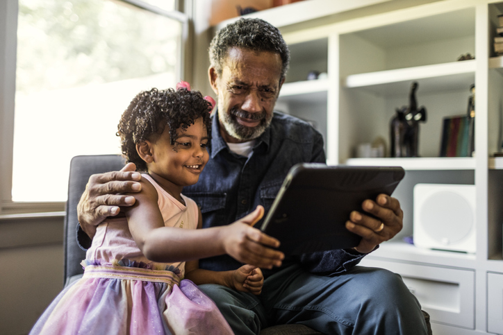 Grandfather shows his granddaughter the digital kids savings account he opened on a tablet. 
