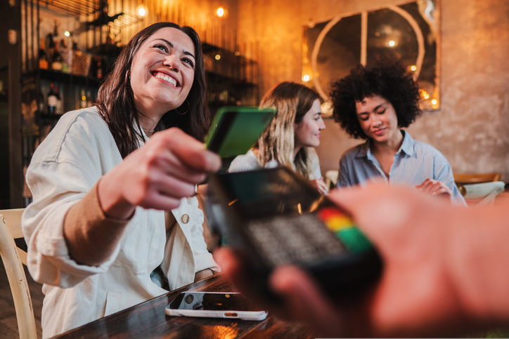 Young happy woman uses her credit card at restaurant, maintaining her healthy credit score.