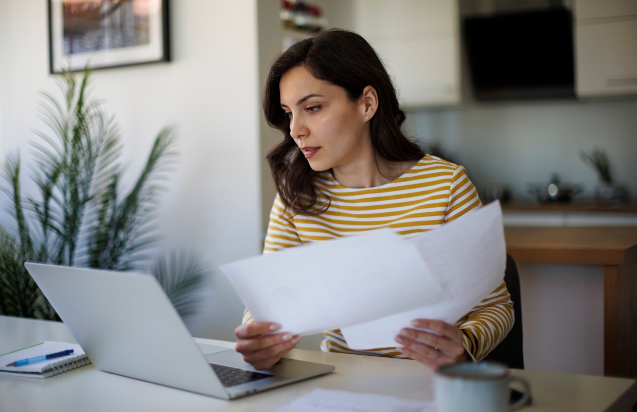 A woman on her laptop holding documentation needed to apply for a HELOC