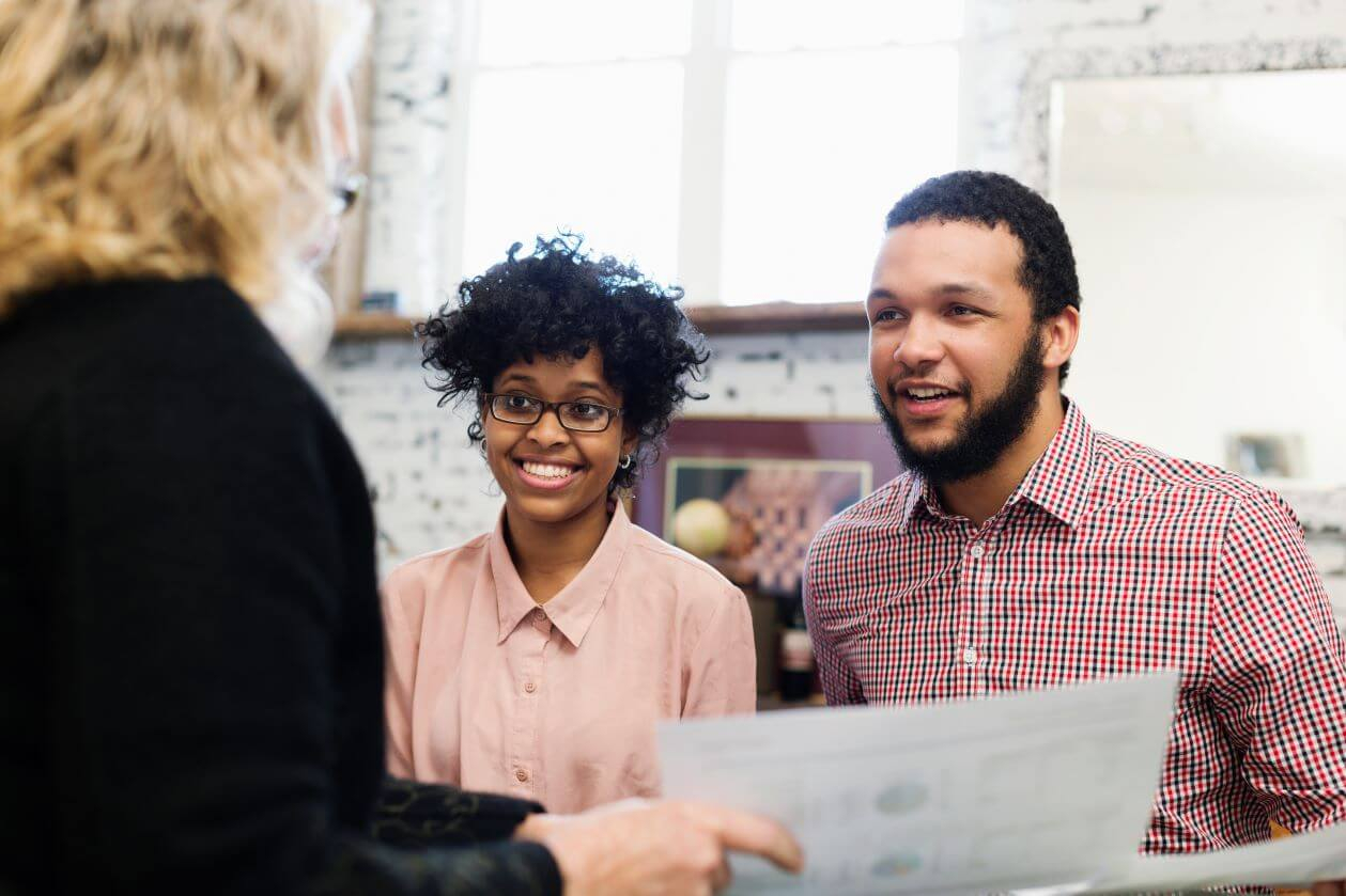 Happy young couple puts bid on their dream home with real estate agent.