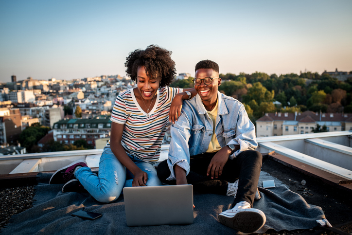 young couple sits on their condominium rooftop exploring HELOC loan limits online on their laptop.