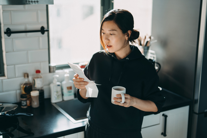 Woman reviews her bank statement in her kitchen to find any financial fees.