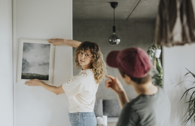 Woman happily hangs painting in new home thanks to first-time homebuyer guide.