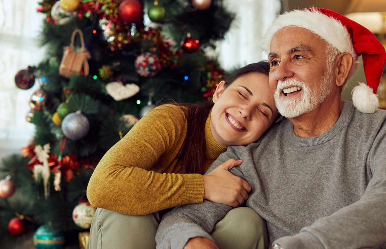Adult daughter thanks for dad, who is wearing a Santa hat, for a financial gift.