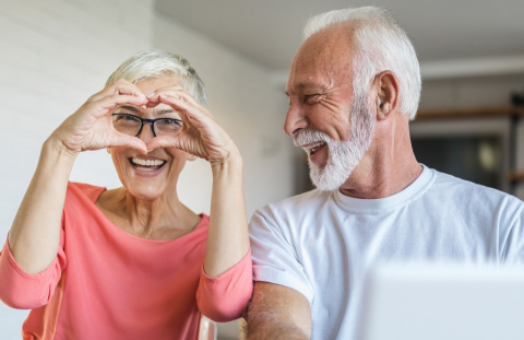 Older couple happily looks at their credit union accounts on their laptop while wife makes heart sign.