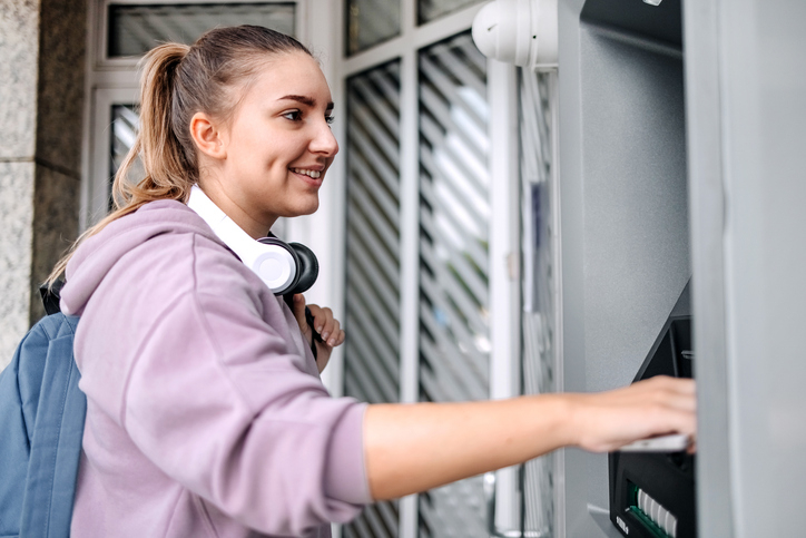 Young woman happily looks at her credit union checking account balance at an ATM. 