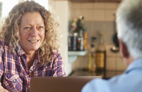 Middle-aged woman talks to her husband about financial planning in their kitchen.