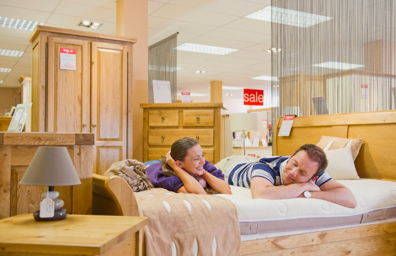 A couple lies on a mattress at a furniture store having a sale