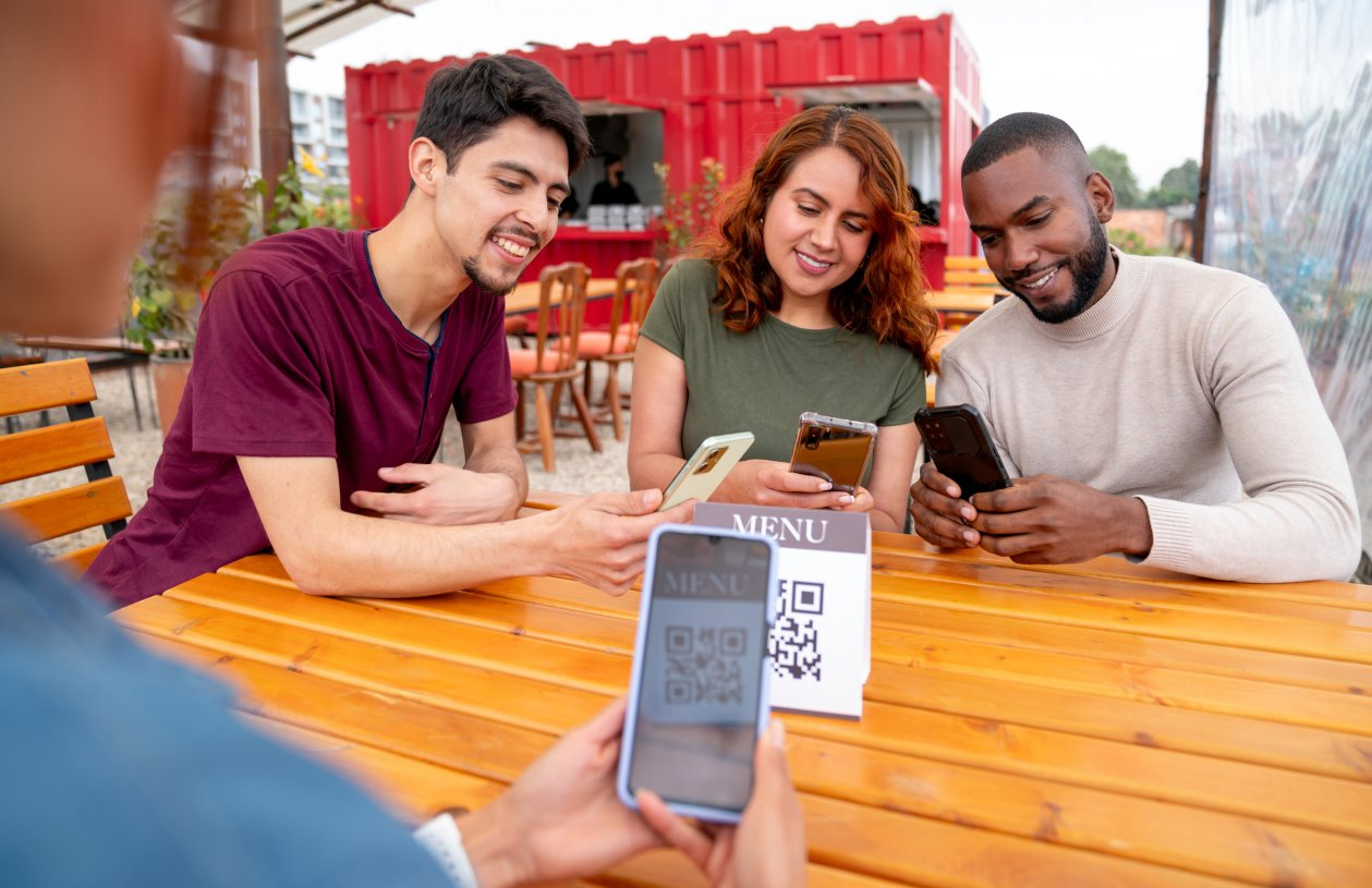 Three friends scan a QR code to access a menu at a restaurant
