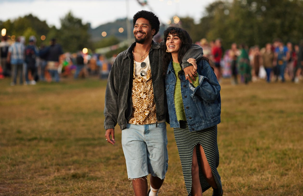 A couple walking through a park with a music festival happening behind them