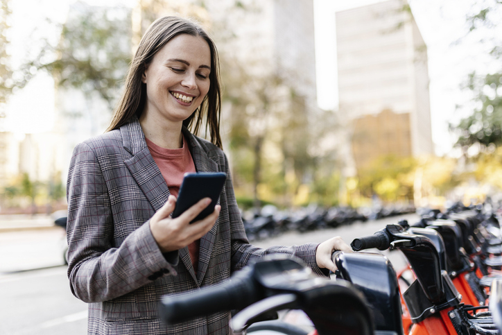 A woman looks at her phone outside while standing next to an electric scooter