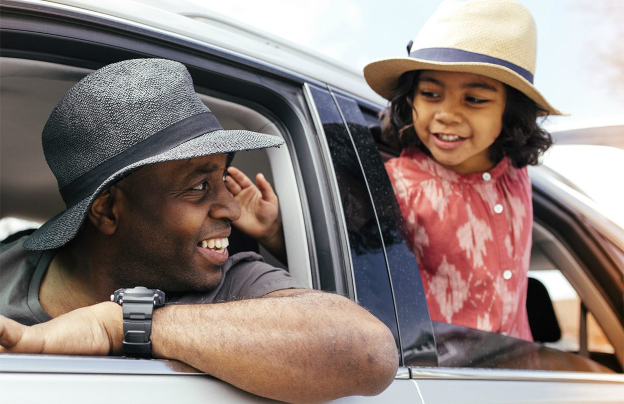 Father and daughter driving in car with windows open on a summer road trip
