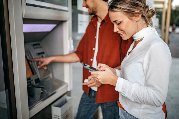 Young couple happily gets cash from their free high-rate checking account at an ATM.