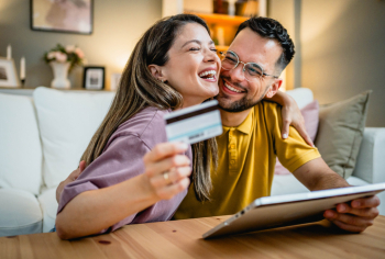 Young couple happily looks at their credit card and credit card account on their laptop, avoiding hidden fees by knowing terms and conditions.