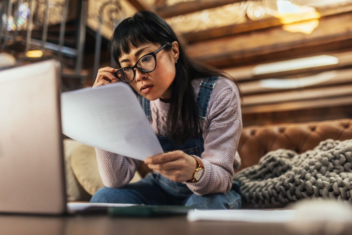 A woman touches the frame of her glasses while looking at a paper loan document 