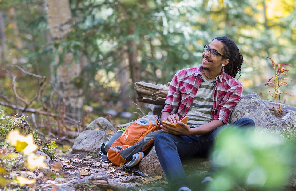man out in the woods writing in a journal about personal finance