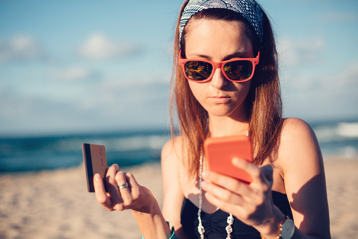 Young woman on beach uses her smartphone to quickly report a money scam on her smartphone to the U.S. Federal Trade Commission.