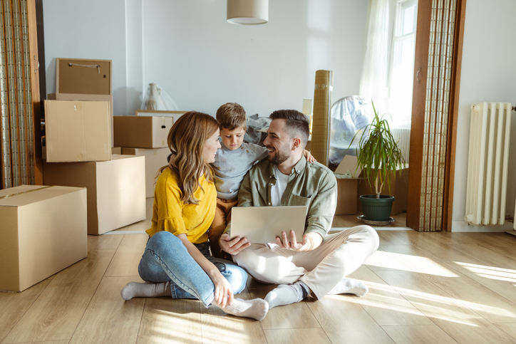 Young married couple sitting among moving boxes show a picture of new home on their laptop after navigating the home loan application process.